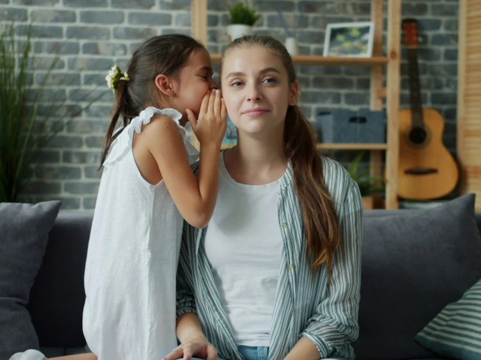 Girl whispers a secret into a woman's ear